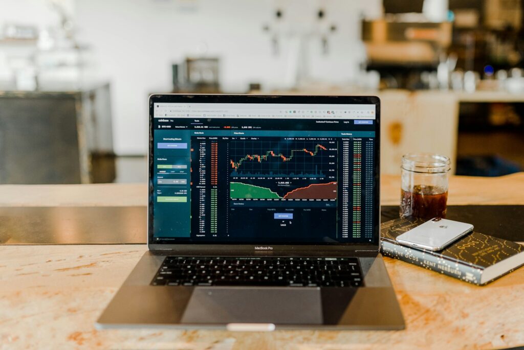 Imagem de uma mesa de trabalho com um computador exibindo a tela de investimentos, destacando gráficos e dados financeiros. A cena transmite a ideia de monitoramento e análise cuidadosa das finanças pessoais ou profissionais.