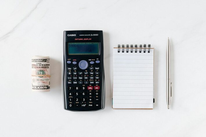 Itens essenciais para planejar sua reserva de emergência: dinheiro, bloco de notas, calculadora e caneta.